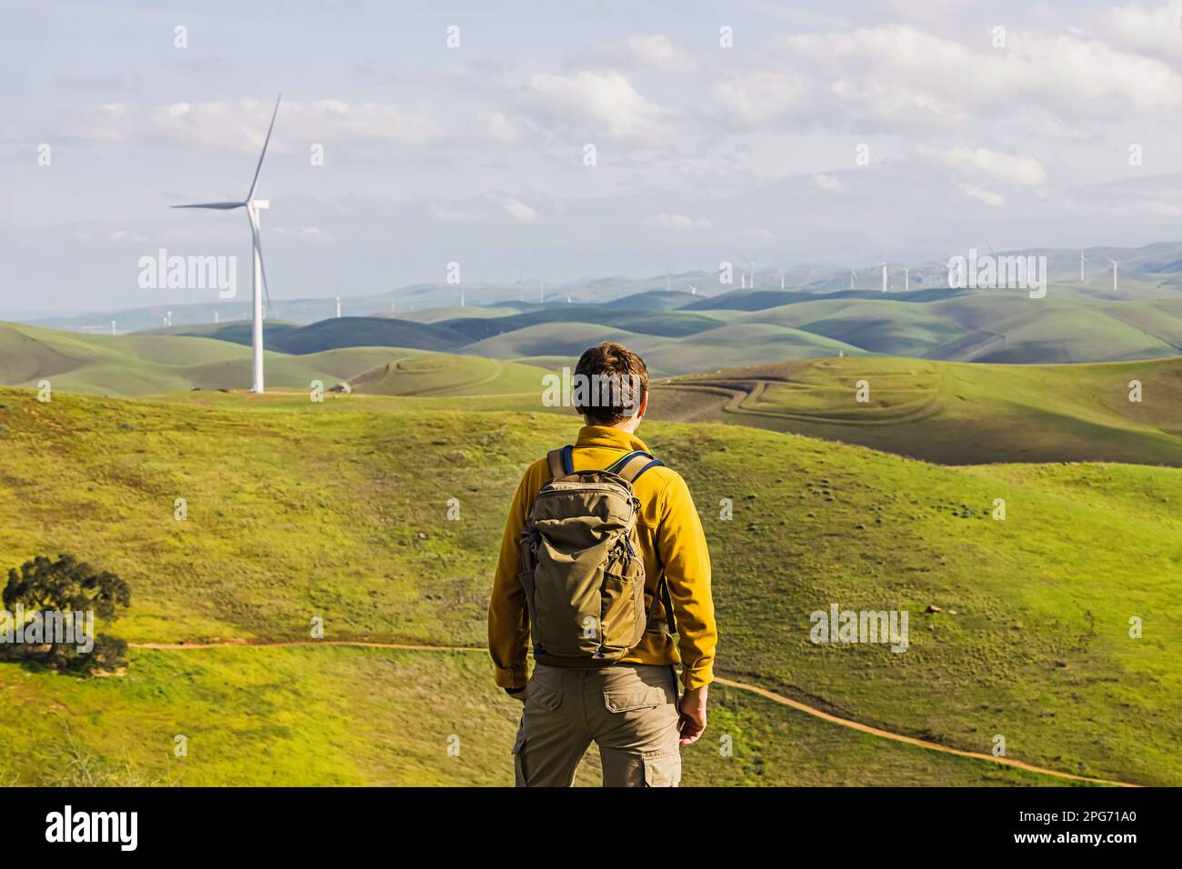 Uomo che guarda sul mulino a vento tra verdi colline, vista dal retro Foto Stock