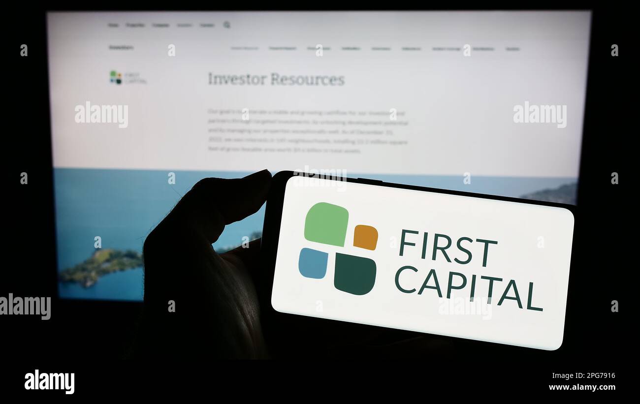 Persona che tiene il cellulare con il logo della società immobiliare canadese prima CAPITALE REIT sullo schermo di fronte al sito web. Messa a fuoco sul display del telefono. Foto Stock