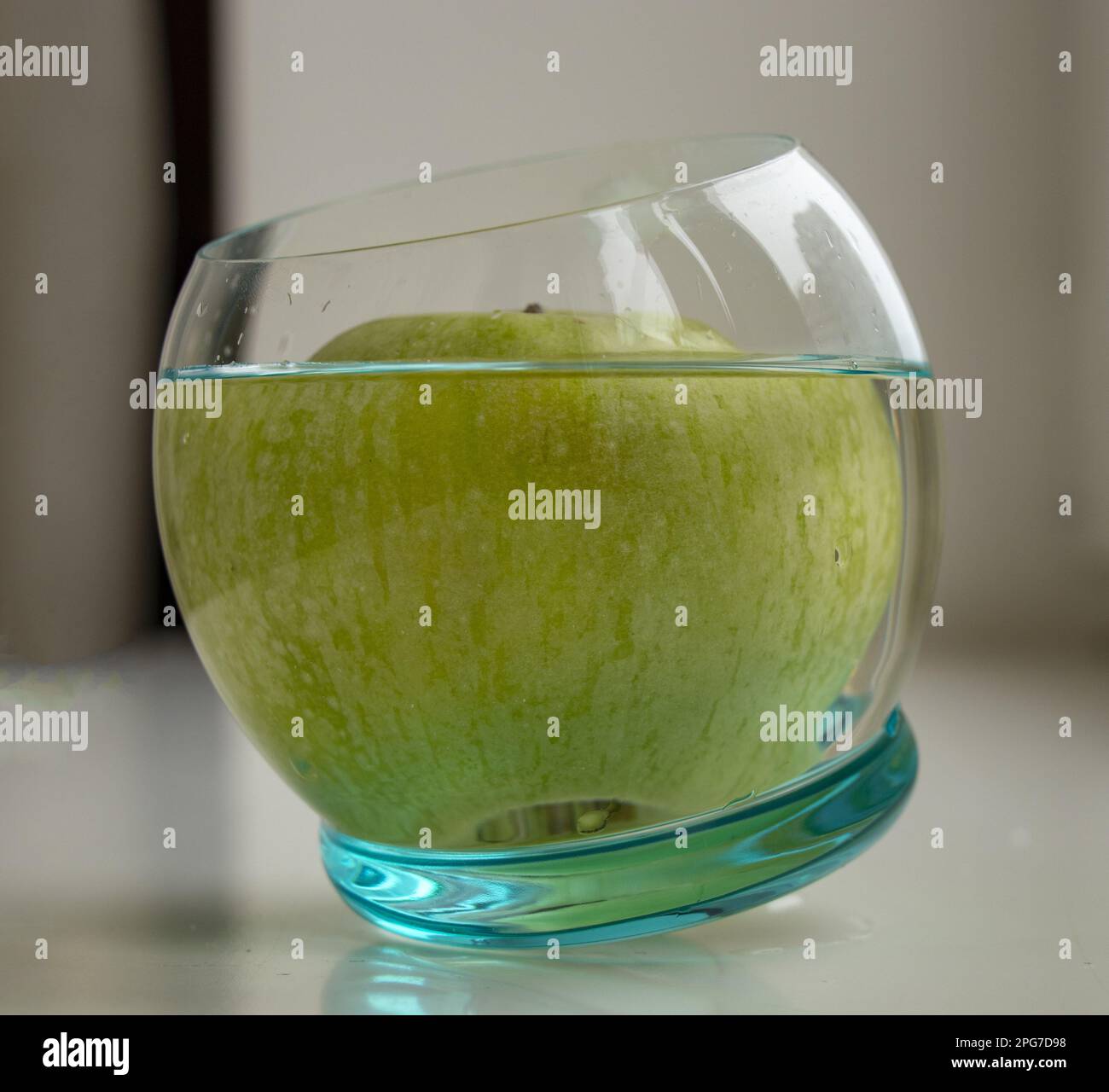 Una mela verde in un bicchiere d'acqua su sfondo chiaro Foto Stock