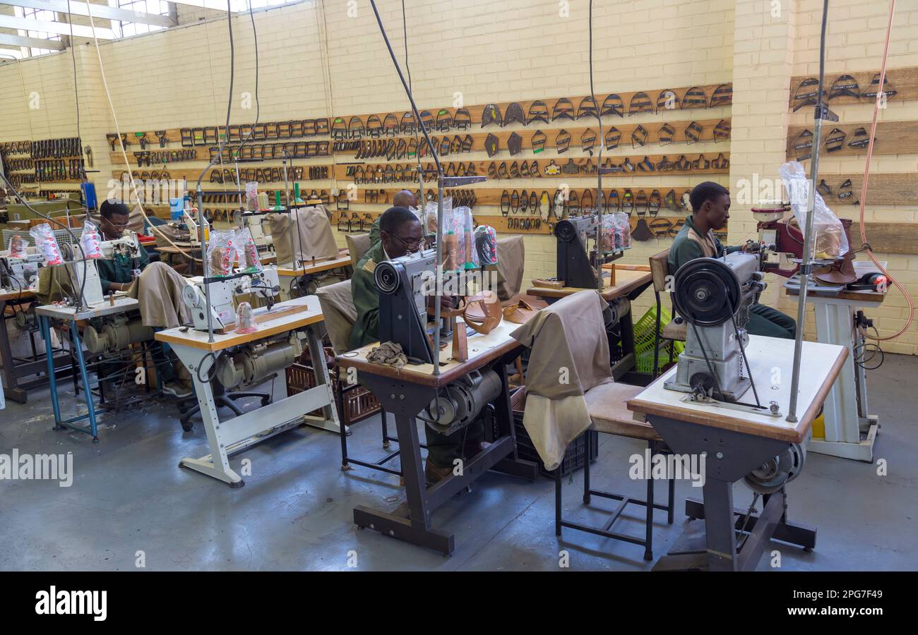 Uomo che indossa occhiali in una fabbrica di scarpe in pelle che utilizza una macchina di cucitura per creare tomaie in pelle Foto Stock