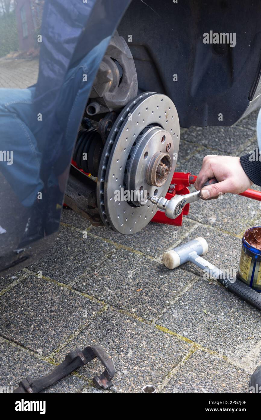 Sostituzione di un vecchio disco del freno con un nuovo disco del freno da parte di un meccanico con attrezzi speciali su una vettura per mantenere una frenata sicura. Foto Stock