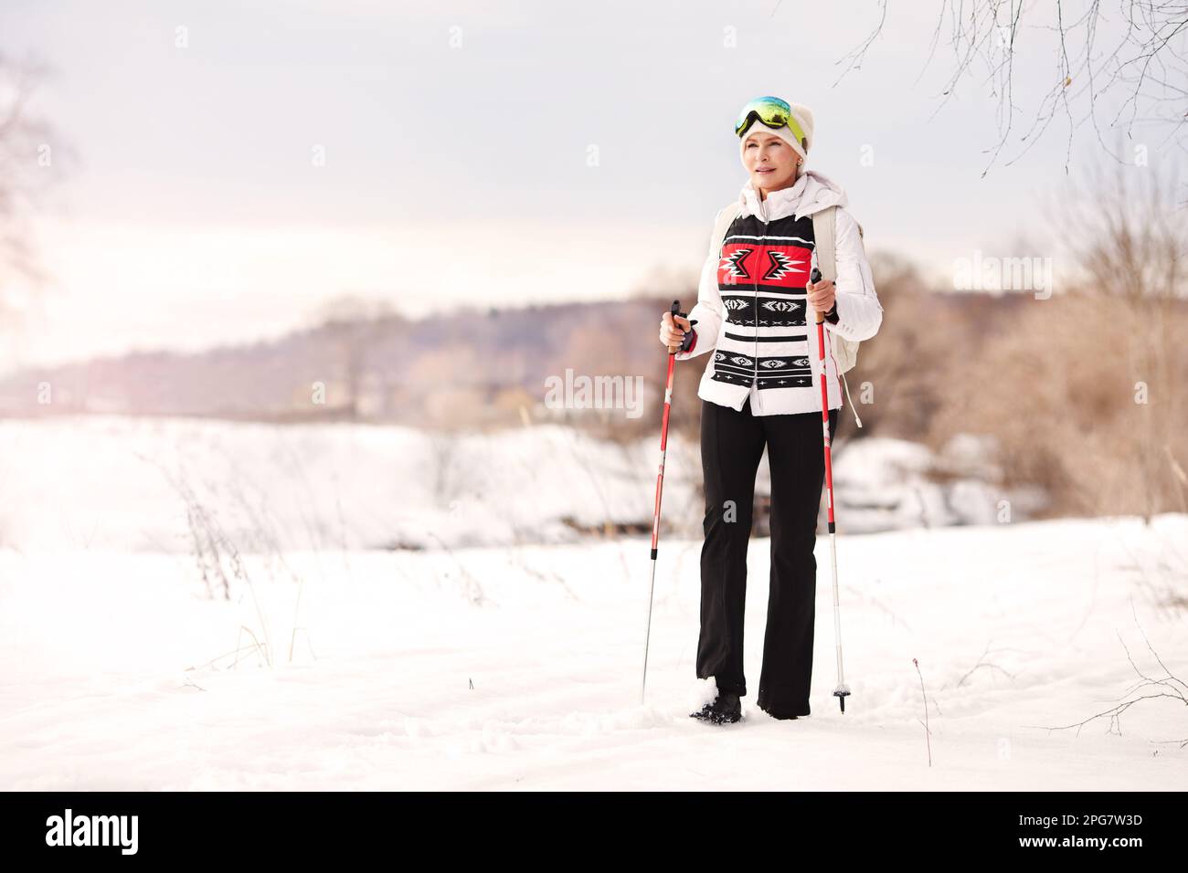 Felice donna anziana cammina con bastoni da nordic walking su sfondo bianco di neve e natura. Sport attivo stile di vita invernale Foto Stock