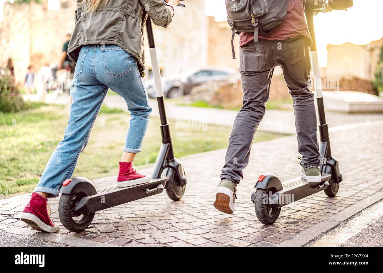Coppia milleniale in sella a scooter elettrici nel parco urbano - studenti di Genz che utilizzano un nuovo mezzo di trasporto ecologico - Green eco Energy Concept Foto Stock