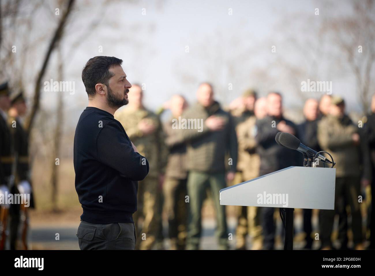 Moschun, Ucraina. 21st Mar, 2023. Il presidente ucraino Volodymyr Zelenskyy rappresenta l'inno nazionale durante una cerimonia presso il sito commemorativo degli Angeli della Vittoria, 21 marzo 2023 a Moschun, Kyiv Oblast, Ucraina. Credit: Foto piscina/Ufficio stampa presidenziale ucraino/Alamy Live News Foto Stock