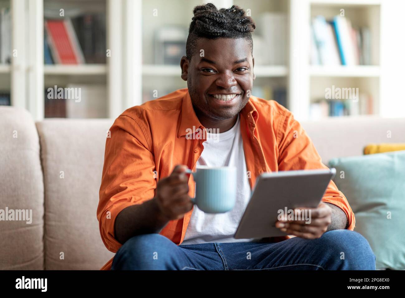 Ragazzo africano positivo rilassarsi a casa, tenendo tablet e tazza Foto Stock