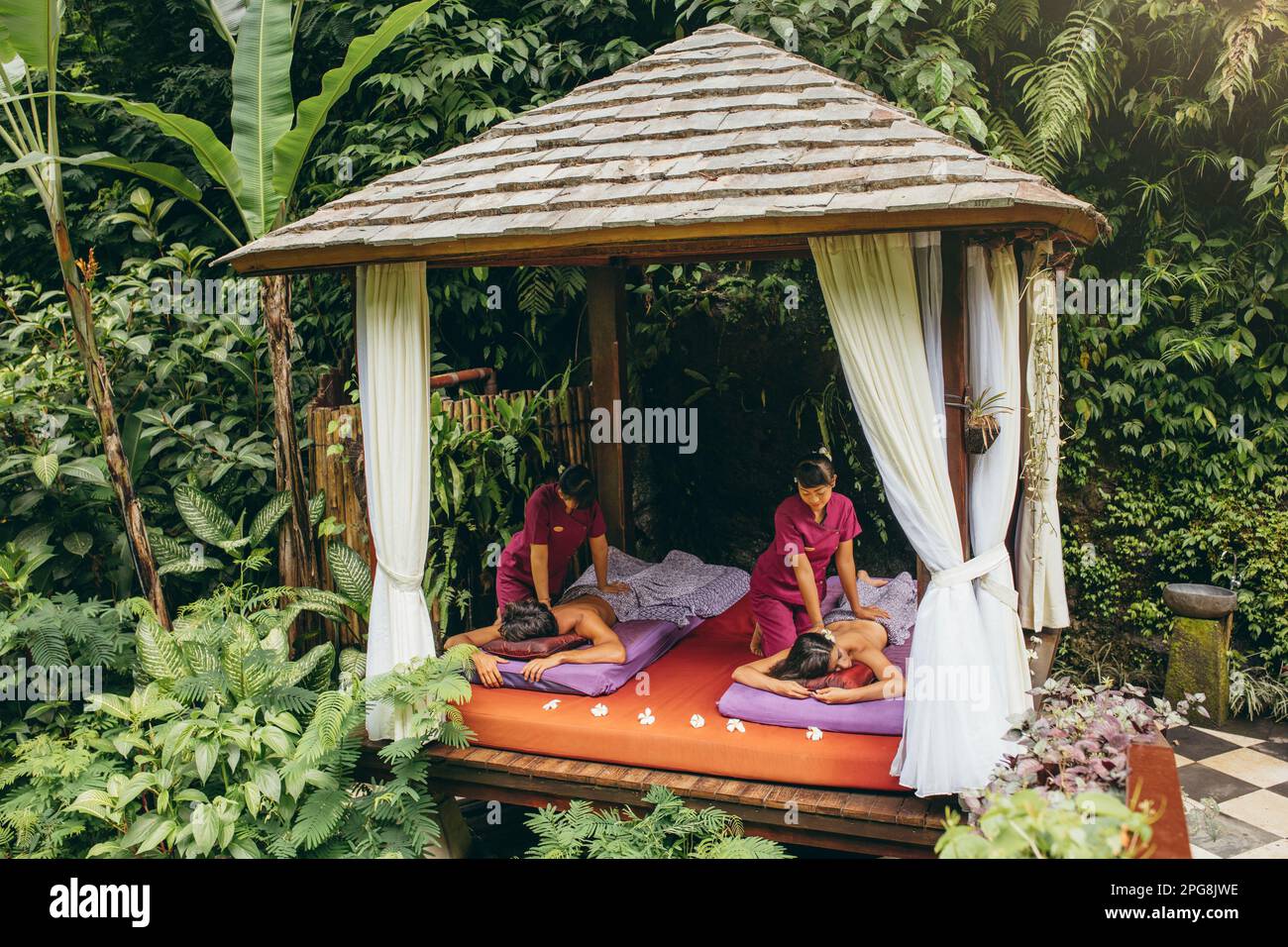 Centro termale all'aperto nel resort di lusso. Centro massaggi circondato da alberi con coppia che riceve massaggio corpo. Foto Stock