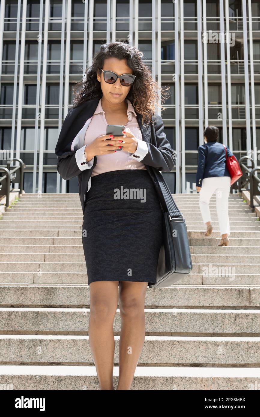 Giovane donna latino-americana che usa il suo smartphone all'aperto. Uomo d'affari che lavora mentre cammina. Foto Stock