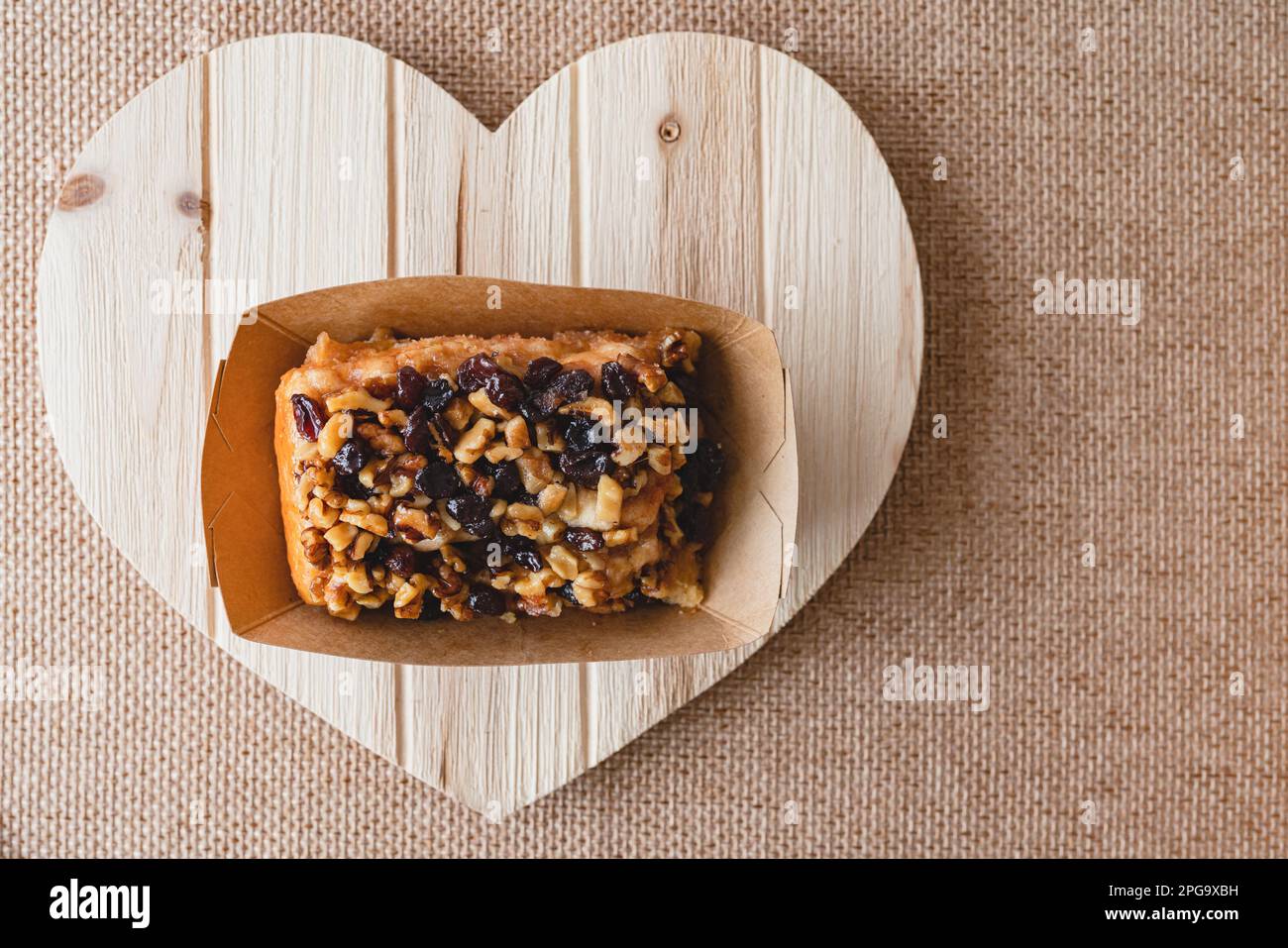 Uva passa Noce cannella rotolo primo piano su un bordo di legno a forma di cuore, piatto giacitura con spazio copia Foto Stock