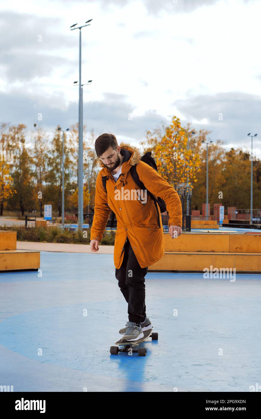 Un giovane adulto elegante e casual a tutta altezza in skateboard in movimento presso lo skatepark, vista laterale Foto Stock