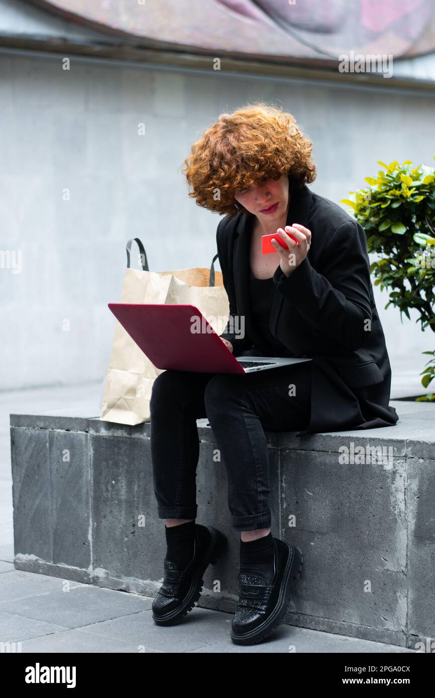 Una persona non binaria che legge i numeri della carta per entrare nel commercio in linea per fare alcuni acquisti Foto Stock