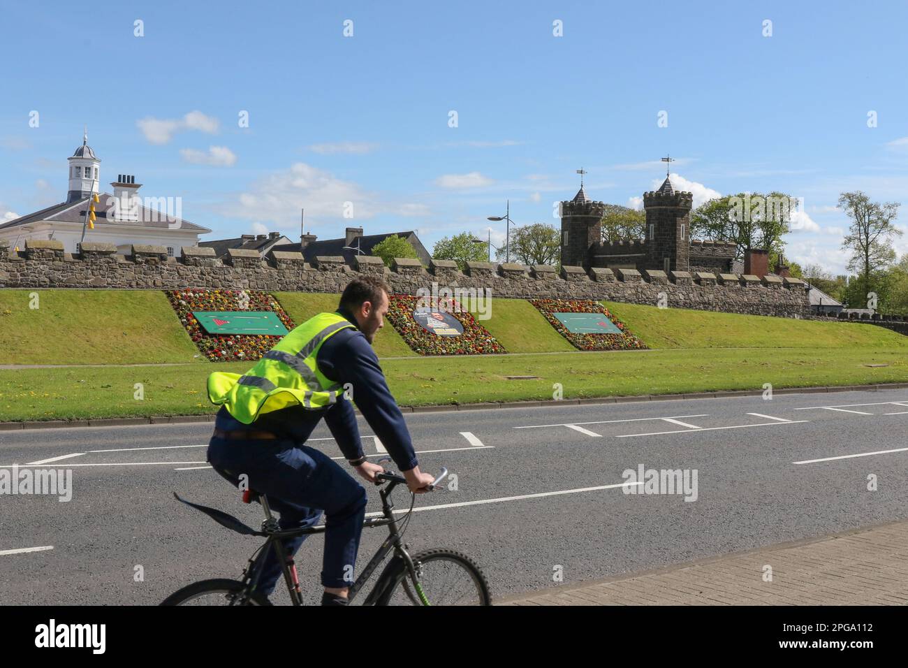In primavera, il ciclista passa accanto alle aiuole di Antrim, Irlanda del Nord, con il vecchio tribunale (a sinistra) e il Barbican Gate Lodge (r). Foto Stock