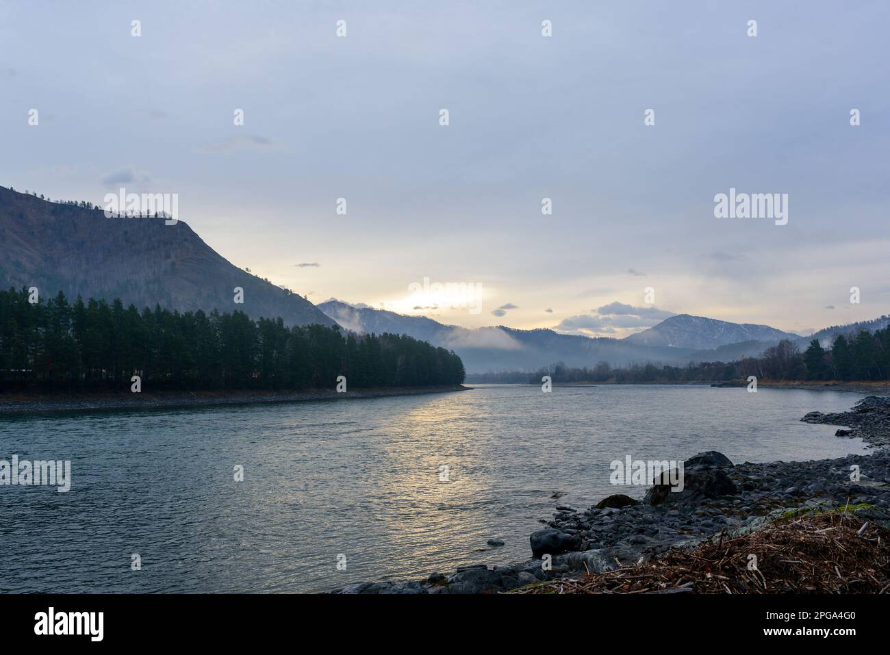 Riva del fiume Katun con pietre al crepuscolo mattutino con il riflesso del sole nascente nell'acqua delle montagne con nebbia Altai a Sibe Foto Stock