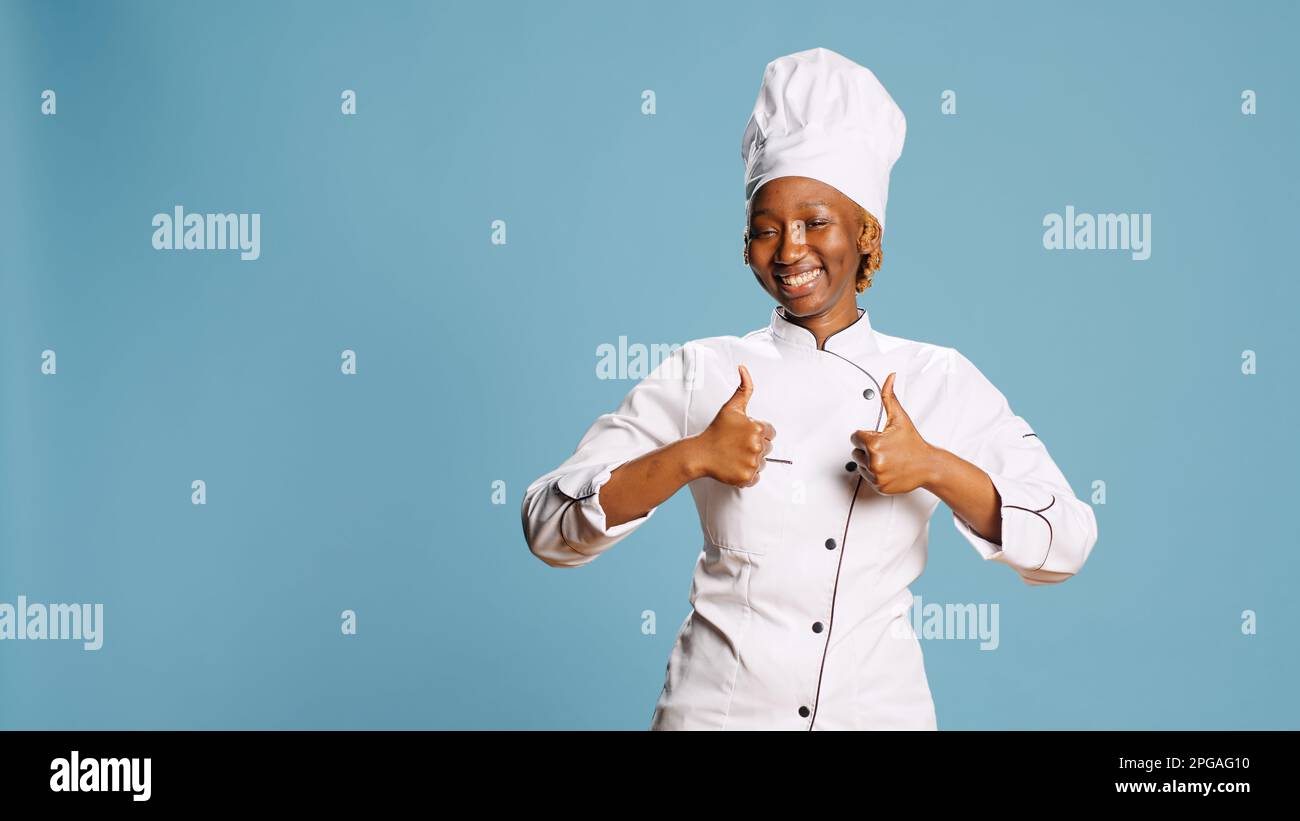 Donna positiva eccitata dando pollici su sulla macchina fotografica, strappando grembiule da cucina ed esprimendo come o simbolo di approvazione. Chef professionista del ristorante che mostra un gesto d'accordo e un successo. Foto Stock