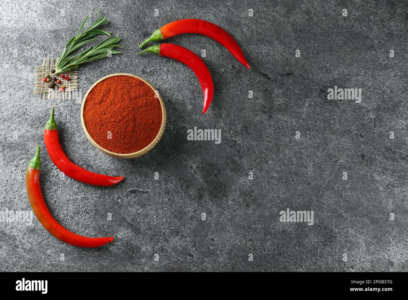 Ciotola di pepe rosso macinato con gli ingredienti sul tavolo grigio, piatto. Spazio per il testo Foto Stock