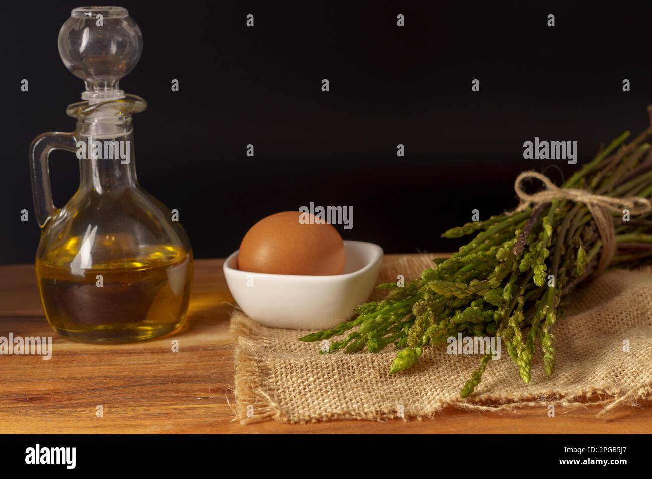 Mazzo di asparagi selvatici su un panno di rafia con un vasetto di olio d'oliva e uova fondo nero Foto Stock