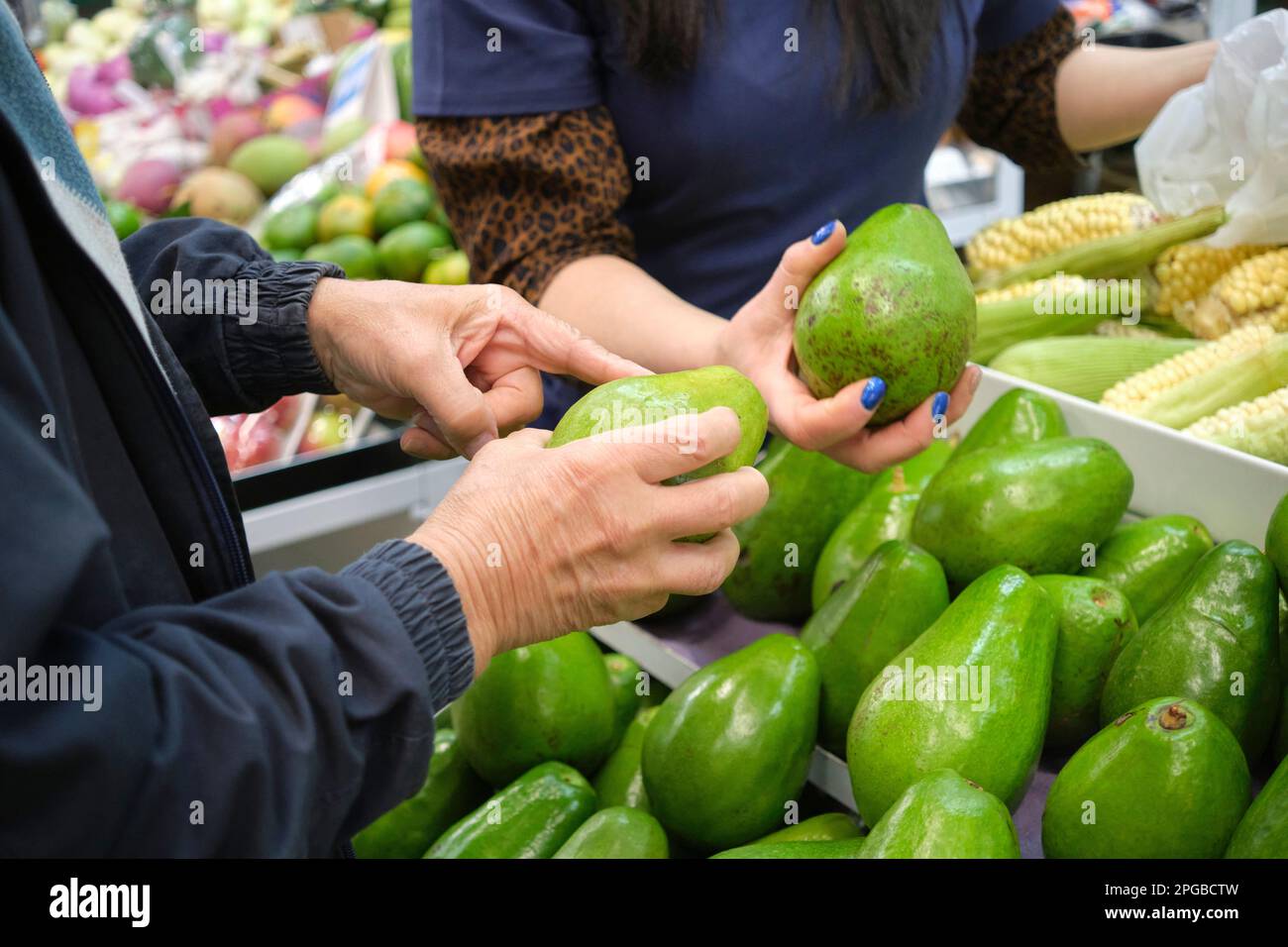 Uomo irriconoscibile che sceglie avocado per comprare in un mercato di verdure. Foto Stock