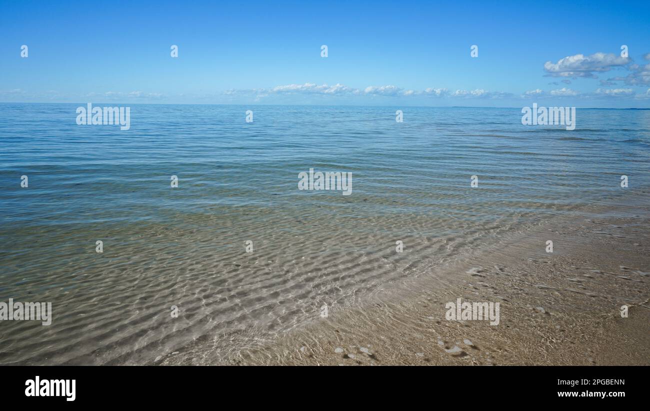 Vista dalla riva, dove le dolci onde lambono la sabbia, attraverso acque cristalline fino all'orizzonte a Burrum Heads, Queensland, Australia Foto Stock