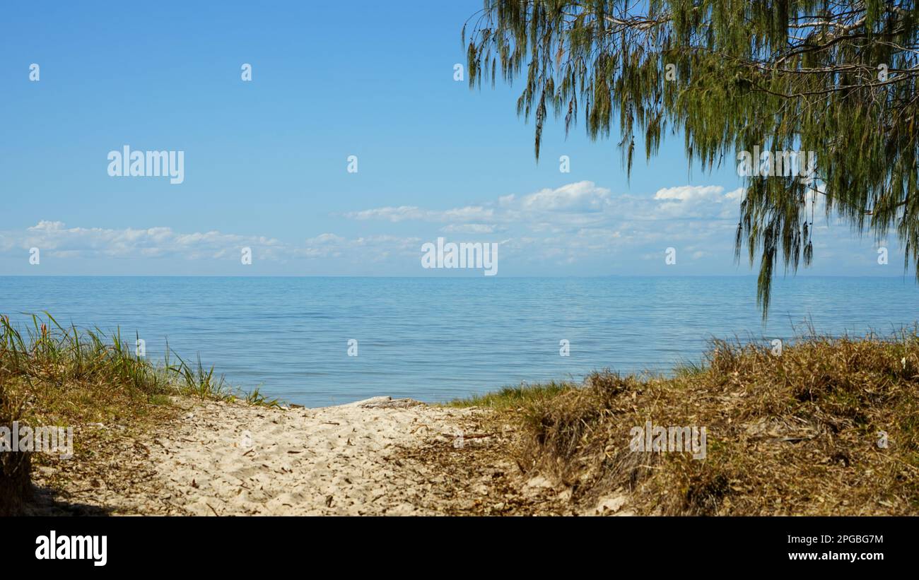 Un sentiero sabbioso sopra una duna conduce a una bellissima acqua blu e calma, che si estende fino all'orizzonte sopra il quale galleggia una collezione di nuvole bianche Foto Stock