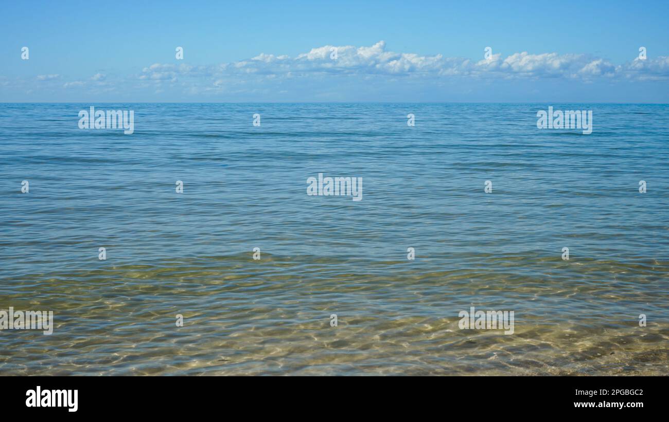 Vista dalla riva, dove le dolci onde lambono la sabbia, attraverso acque cristalline fino all'orizzonte a Burrum Heads, Queensland, Australia Foto Stock