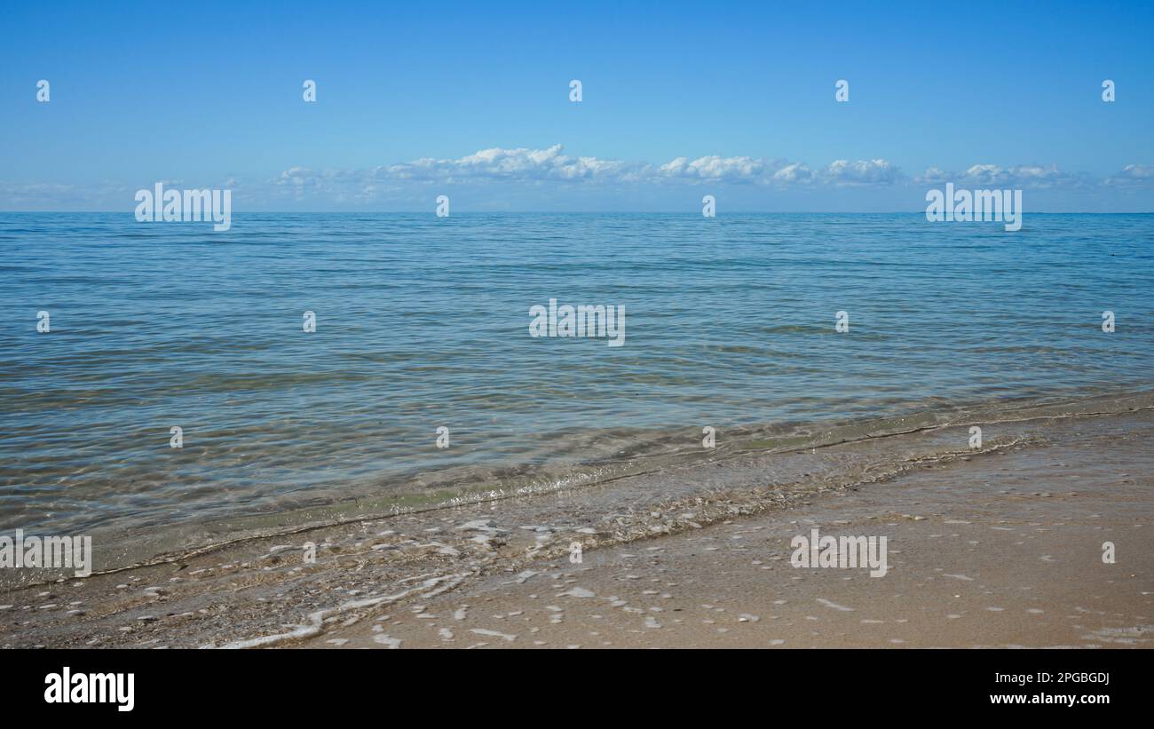 Vista dalla riva, dove le dolci onde lambono la sabbia, attraverso acque cristalline fino all'orizzonte a Burrum Heads, Queensland, Australia Foto Stock