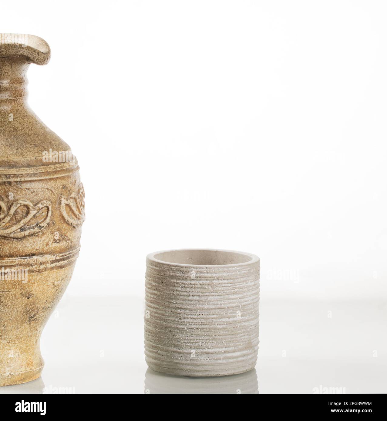 Caraffa di argilla per il vino e un bicchiere di argilla sullo sfondo di uno specchio bianco. Foto Stock