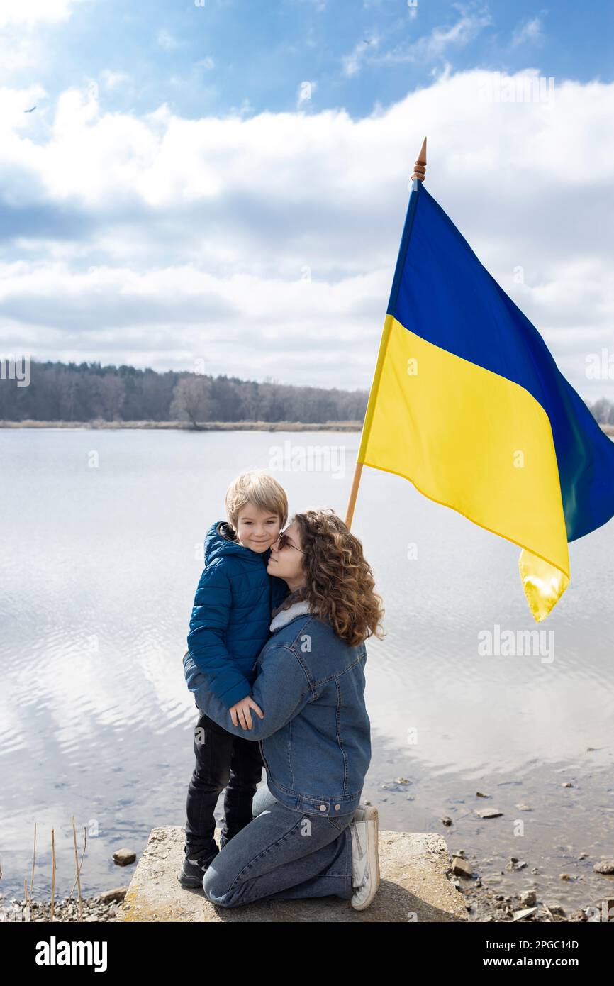 Ragazzo e giovane donna, fratellino e sorella adulta, accanto al lago con bandiera dell'Ucraina. Famiglia, unità, rifugiati, sostegno. Stare con l'Ucraina. stop wa Foto Stock