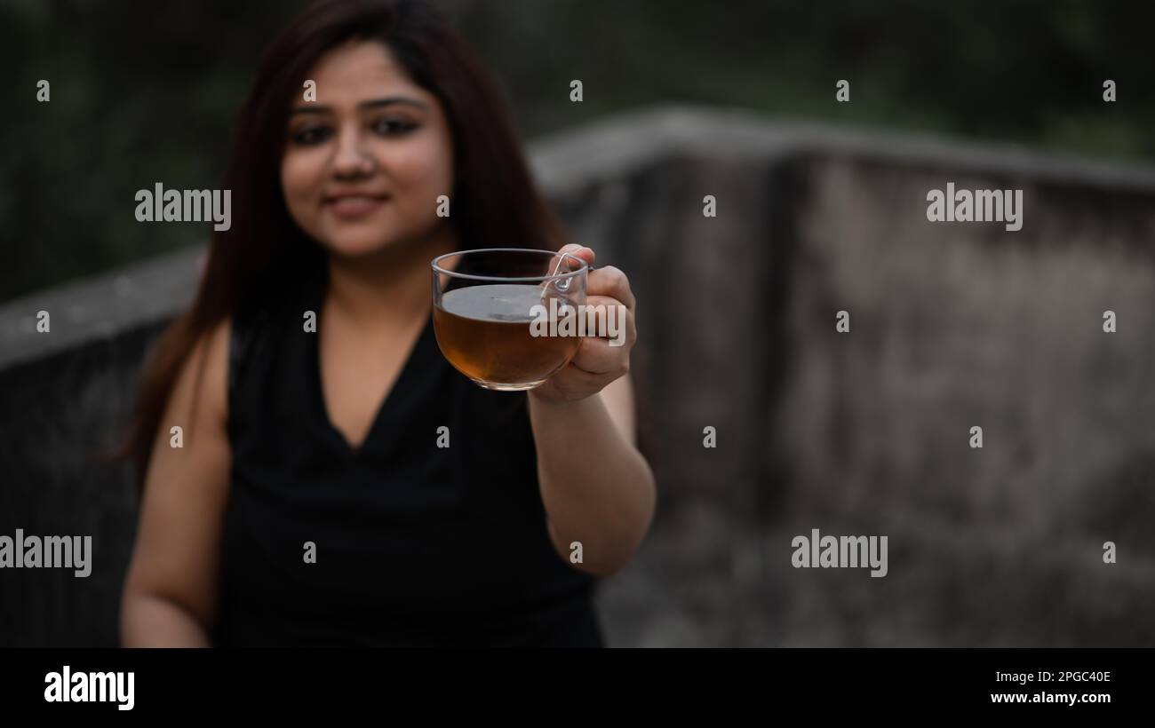 Le donne che si siedono con una tazza da tè in vetro trasparente che offre tè nero Foto Stock