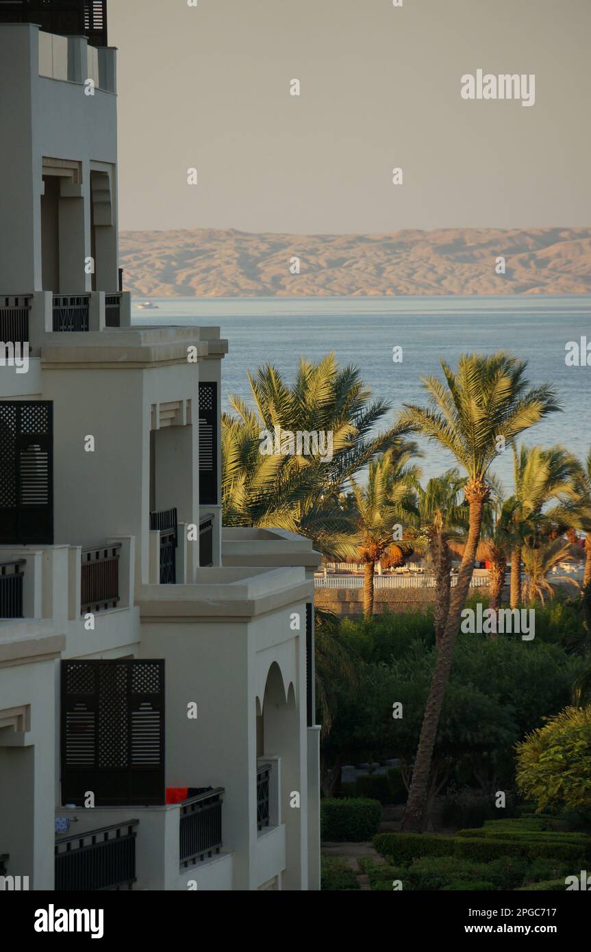 Una vista di un edificio bianco che si affaccia su un pittoresco paesaggio di palme, acqua e colline. Foto Stock