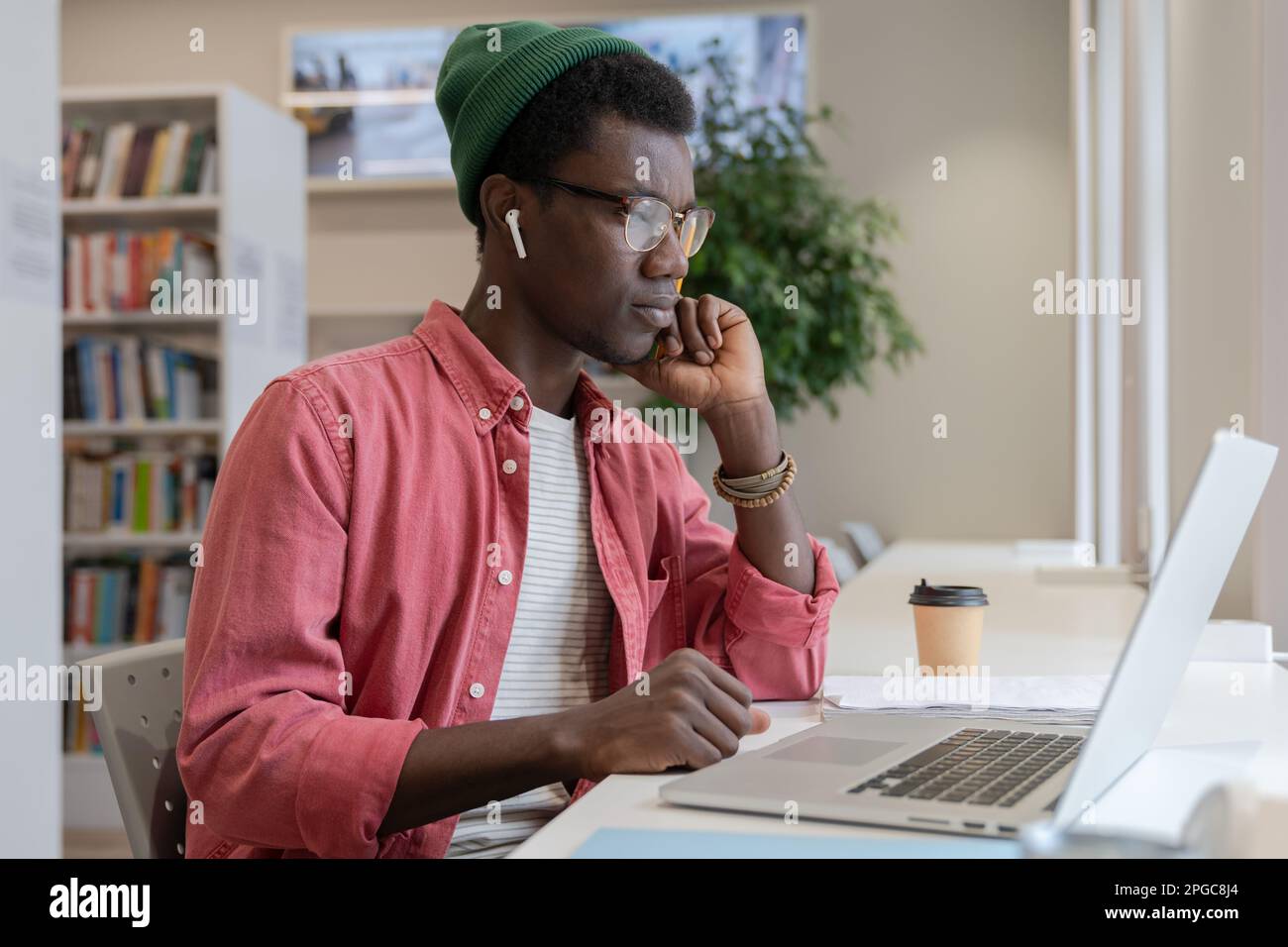Insegnante di tutor di giovane uomo africano focalizzato che guarda il laptop che si prepara per la classe on-line in biblioteca Foto Stock