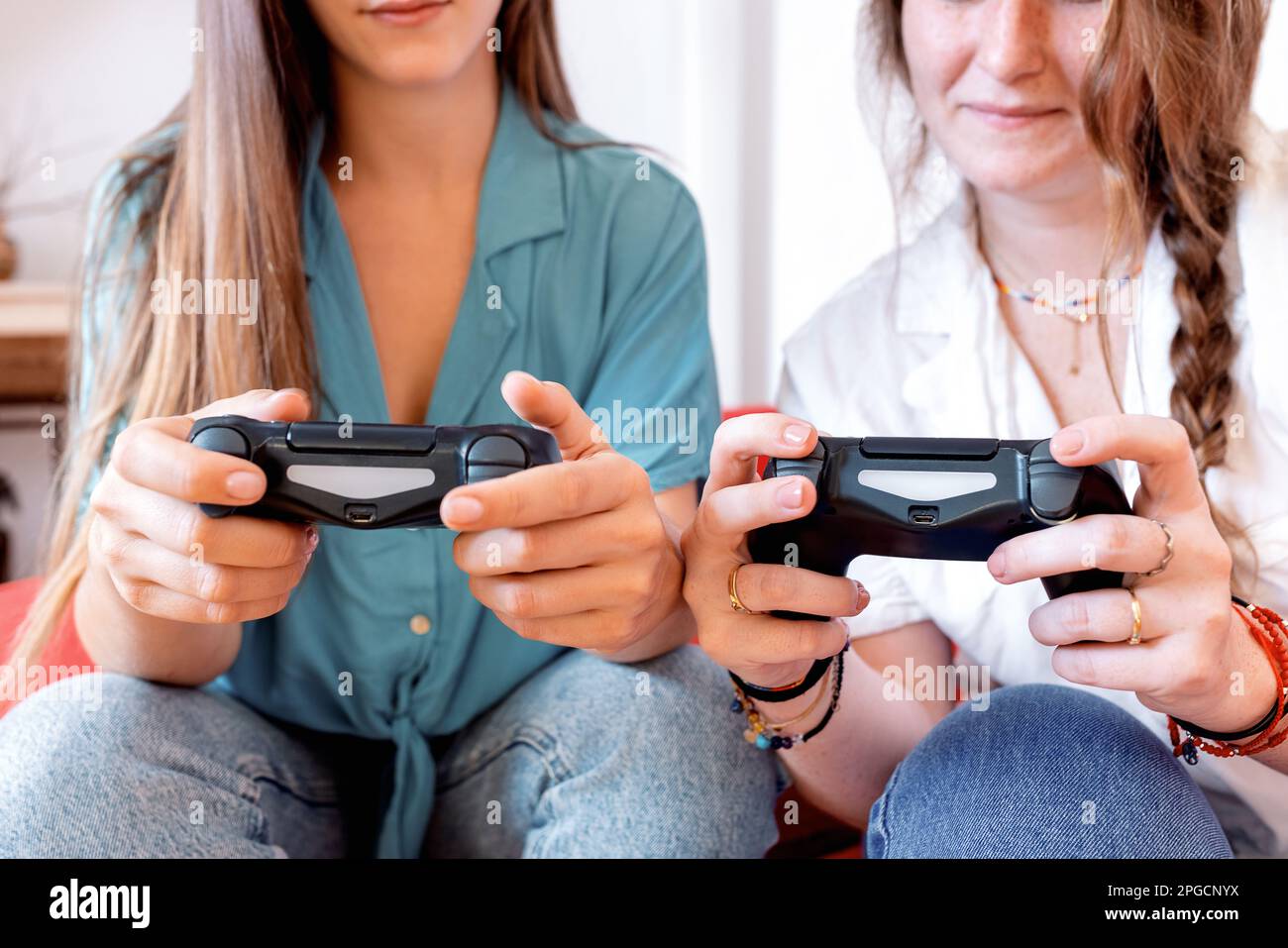 Le amiche femminili sono irriconoscibili e si rilassano su un comodo divano di colore rosso con controller per videogiochi in mano e si divertono con la dur del tempo libero Foto Stock