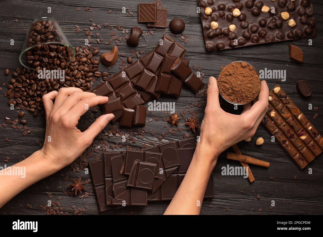 Piatto di cioccolato su sfondo di legno scuro. Dessert al cioccolato in mani femminili su uno sfondo di cioccolato fondente e al latte sparso. Foto Stock