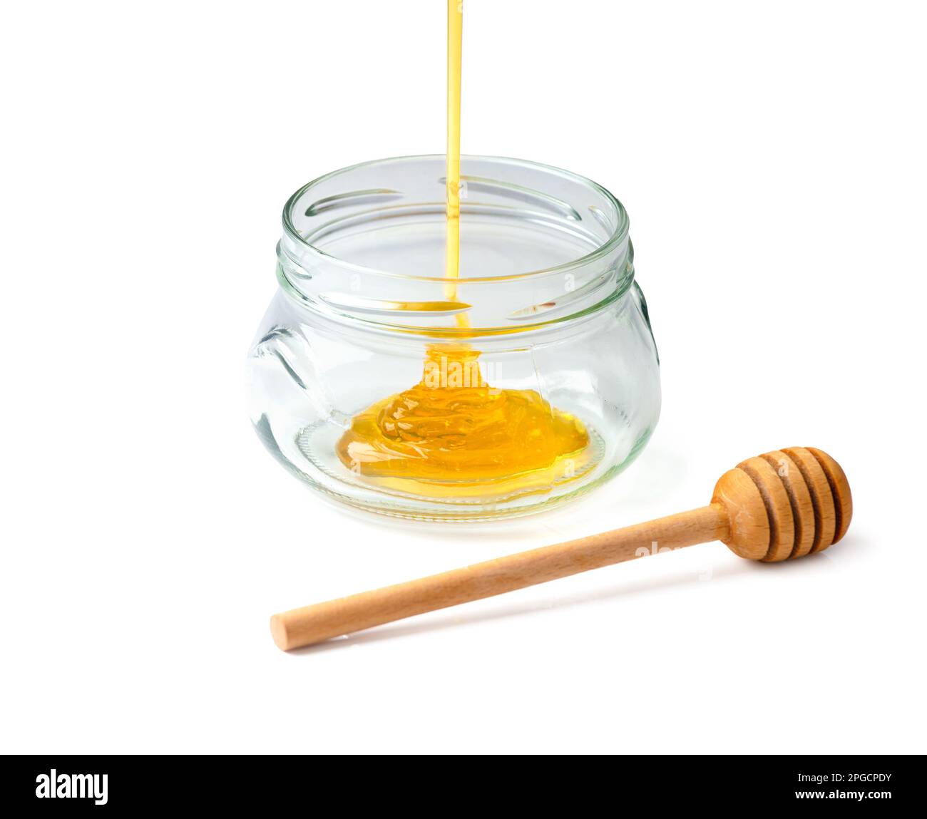 Il miele viene versato in un vaso di vetro aperto. Miele in vaso e un cucchiaia su fondo bianco. Versare miele sull'isolamento. dessert naturali. Alimenti sani Foto Stock