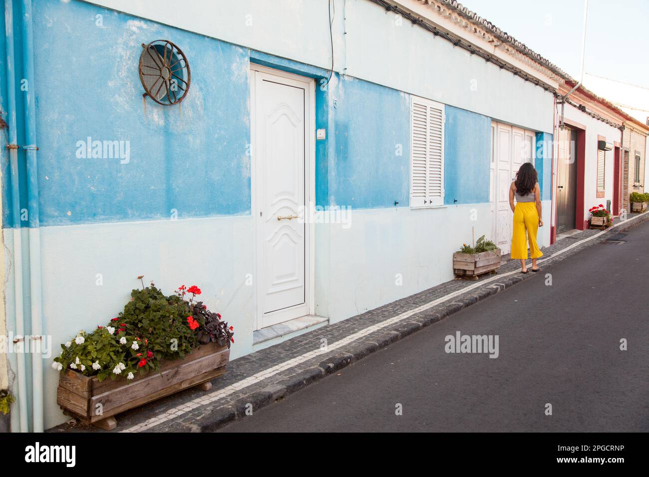 Vista posteriore della giovane donna in abiti estivi in piedi sulla strada circondata da edifici in giornate di sole in Azzorre, Portogallo Foto Stock