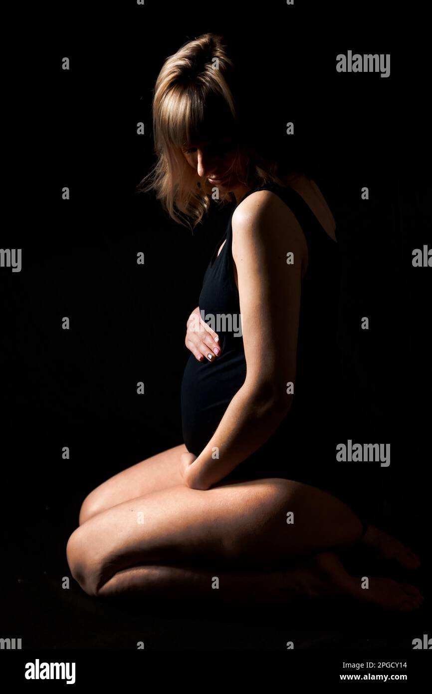 Donna incinta con grande pancia in bodysuit, lingerie su sfondo nero. Sexy ragazza attraente photoshoot in studio. Buona gravidanza, maternità, preparati Foto Stock
