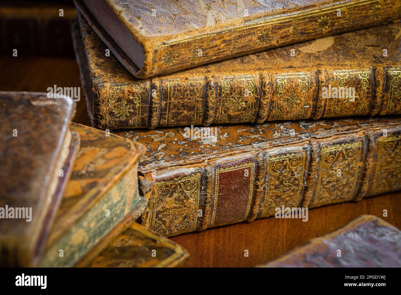Pila di libri antichi con copertina in pelle e ornamenti dorati su un tavolo di legno Foto Stock