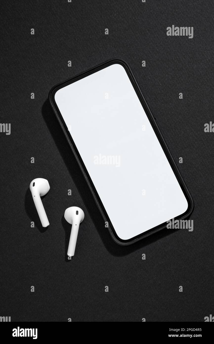 Smartphone con schermo vuoto e cuffie wireless accanto su sfondo grigio scuro Foto Stock