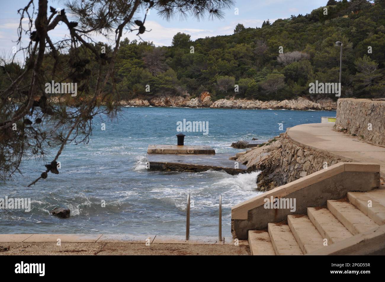 Molo in pietra con arrugginito. Completamente arrugginito dilapidato ferro ormeggio in mezzo al molo di pietra. Pino sulla costa. Foto Stock