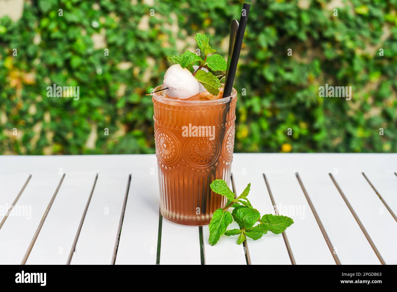 Tè verde ghiaccio con lychee e menta su tavolo di legno bianco contro foglie verdi con spazio copia Foto Stock