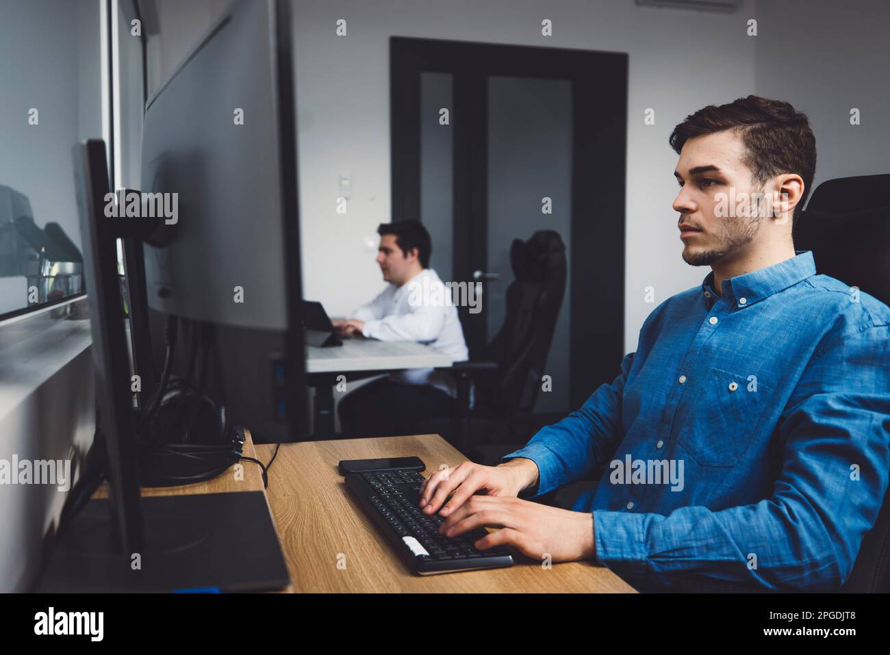 Vista laterale, due programmatori che lavorano in ufficio codificando su computer da tavolo Foto Stock