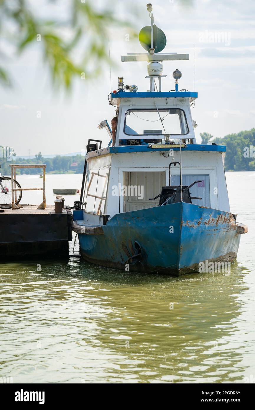 Un vecchio piccolo traghetto attende i passeggeri al porto per attraversare il fiume. Il capitano è in attesa sul traghetto per la partenza. Foto Stock