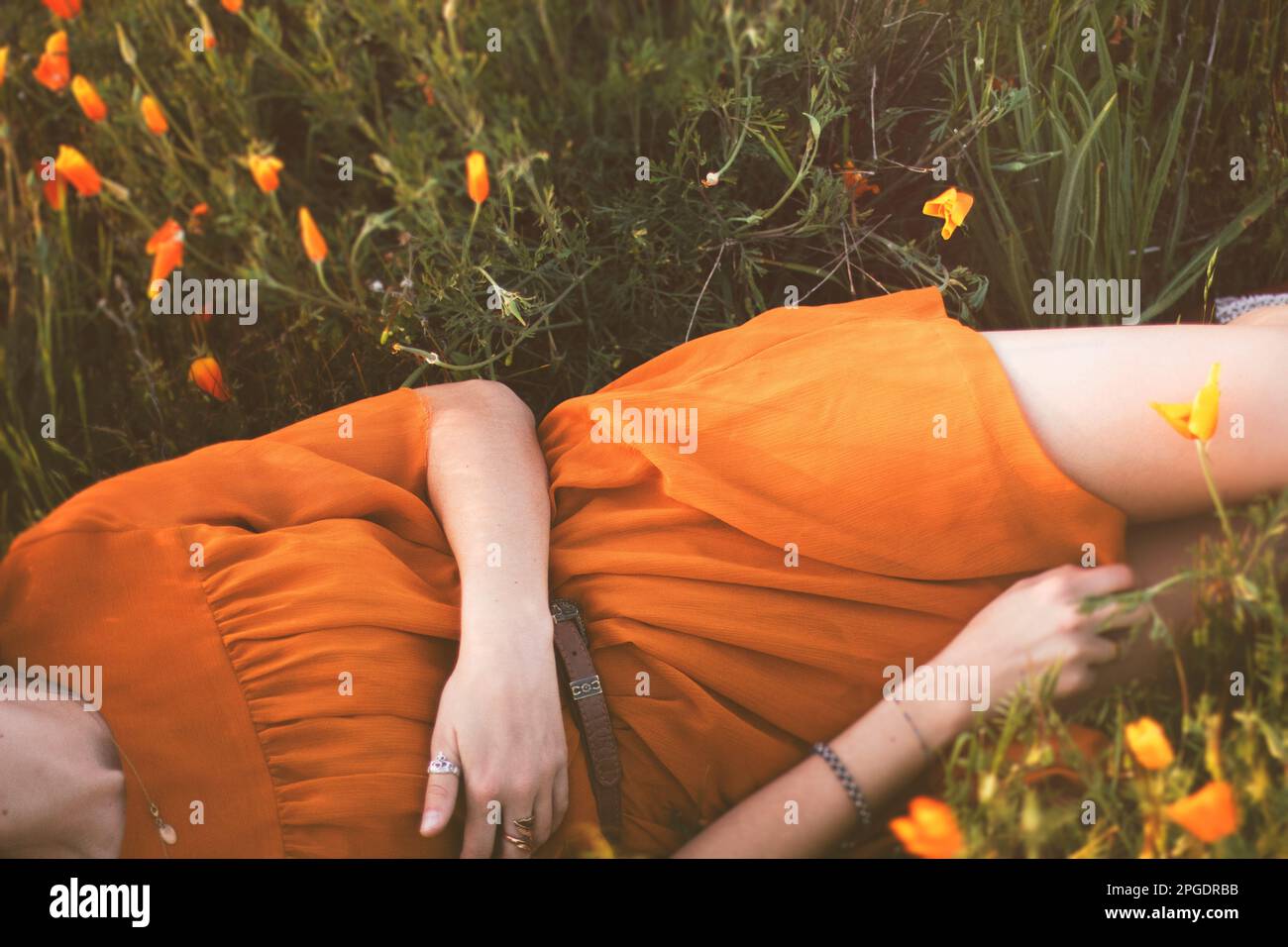 Primo piano di una donna in un abito estivo arancione sdraiato in un prato di papaveri selvatici, USA Foto Stock