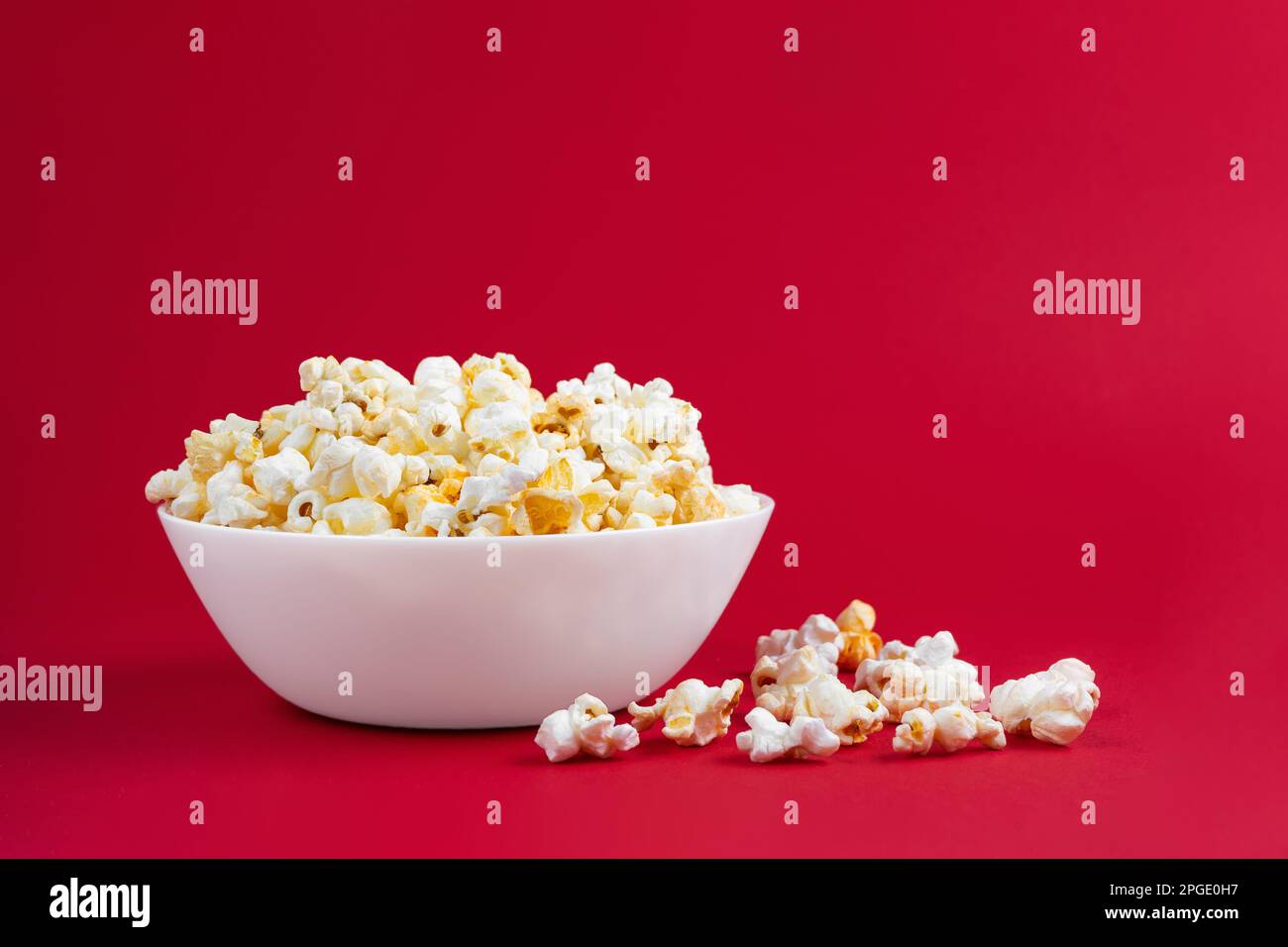 Formaggio saporito popcorn sparso in ciotola bianca isolato su sfondo rosso. Piano di giacitura, vista dall'alto. Fast food, cinema, cinema Foto Stock