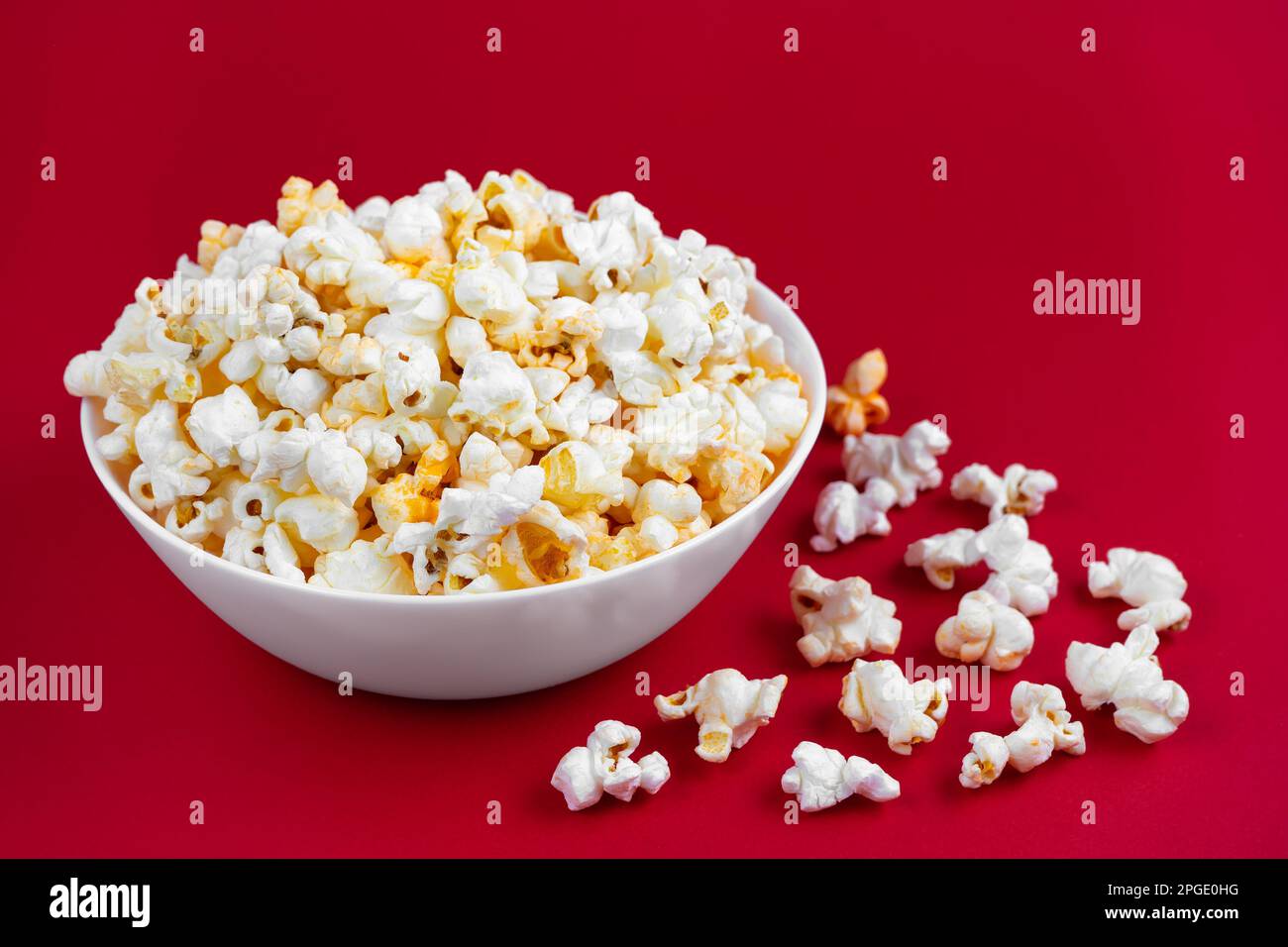 Formaggio saporito popcorn sparso in ciotola bianca isolato su sfondo rosso. Piano di giacitura, vista dall'alto. Fast food, cinema, cinema Foto Stock