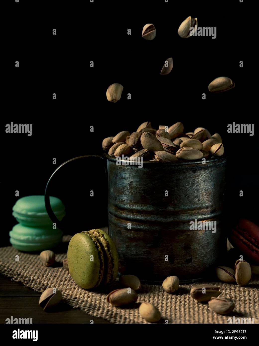 Un contenitore di latta pieno di pistacchi e altri volanti, con macaron accanto ad essi Foto Stock