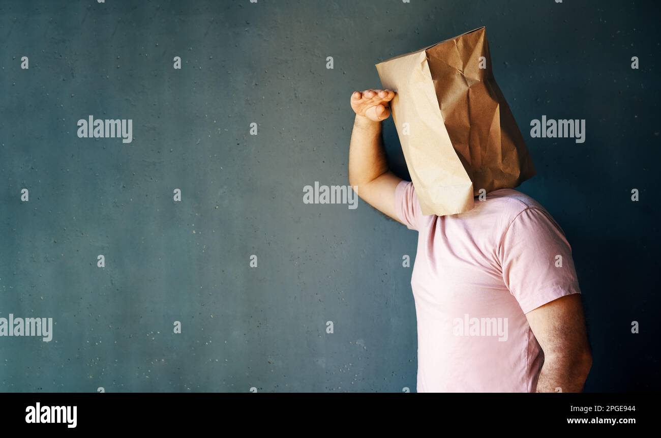 Uomo con un sacchetto di carta sulla testa che guarda lontano distanza su sfondo grigio con spazio di copia Foto Stock