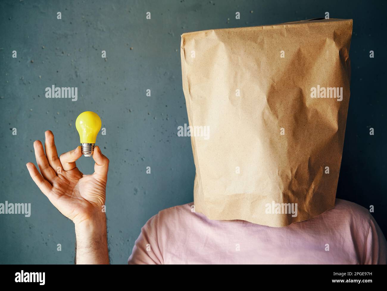 Uomo con un sacchetto di carta sulla testa che tiene in mano la lampadina. concetto di idea con innovazione e ispirazione Foto Stock