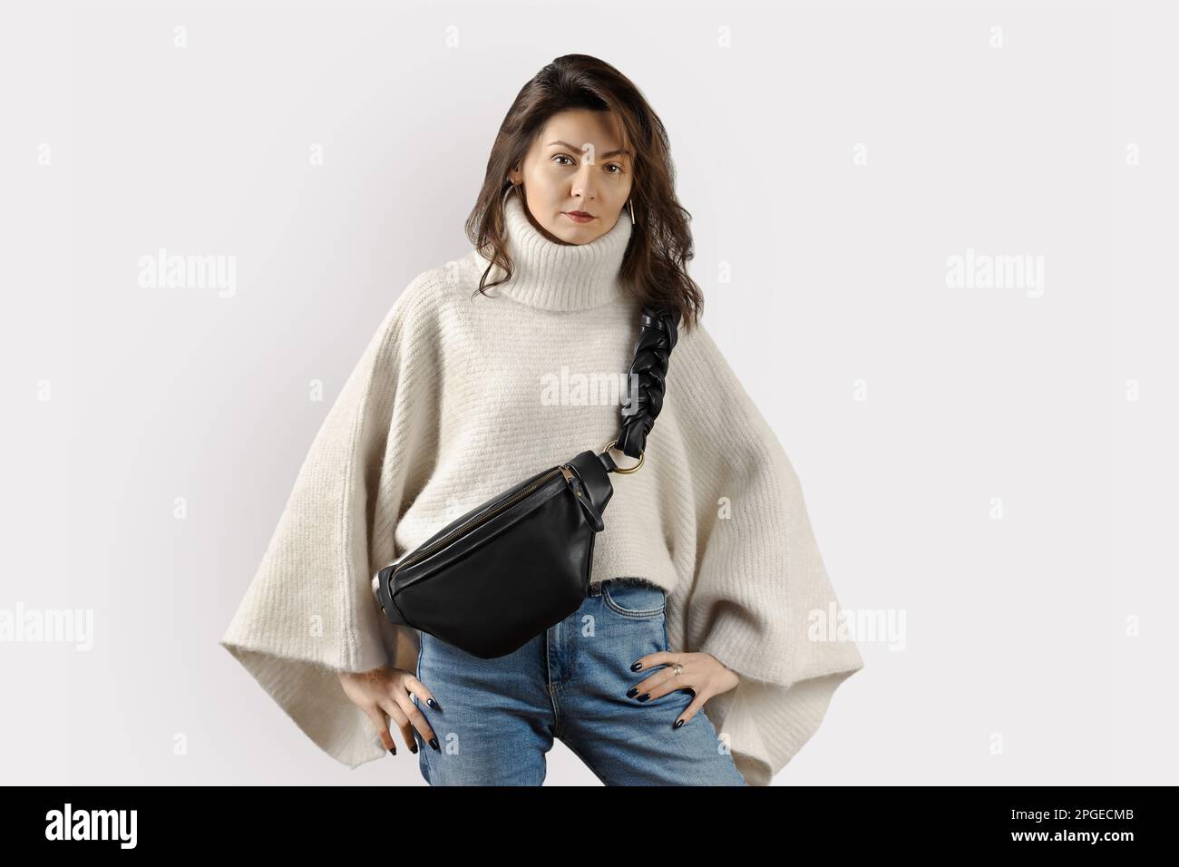Donna che indossa un pullover oversize bianco e un fanny pack in vera pelle nera con tracolla intrecciata. Look alla moda per la stagione invernale Foto Stock