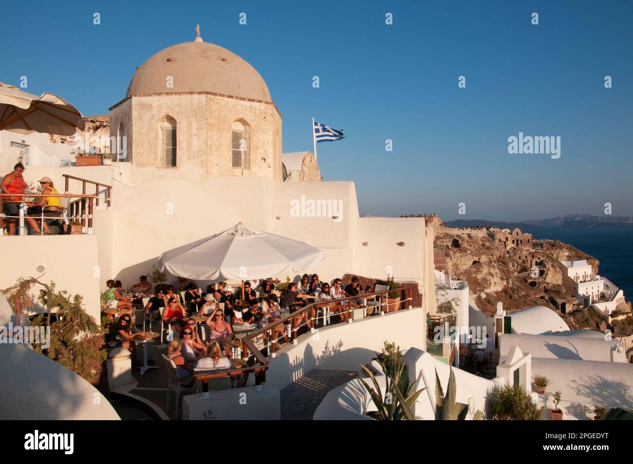 Happy hour sulla terrazza panoramica sul mare in estate con molte persone sedute ai tavoli che guardano il tramonto nel villaggio di Oia, Grecia Foto Stock