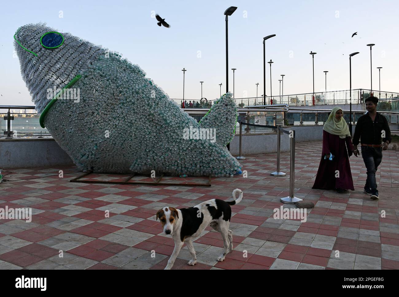 La gente cammina vicino all'installazione del pesce in bottiglia del PET (polietilentereftalato) a Mumbai. I giovani volontari di Change sono noi a creare il PET (polietilentereftalato) bottiglia pesce per creare consapevolezza circa il riciclaggio, più di seimila plastiche sono stati riutilizzati per creare questa gigantesca installazione. Secondo uno studio, entro il 2050 ci sarà più plastica che pesce nel mare e quindi è importante evidenziare il consumismo cosciente. Foto Stock