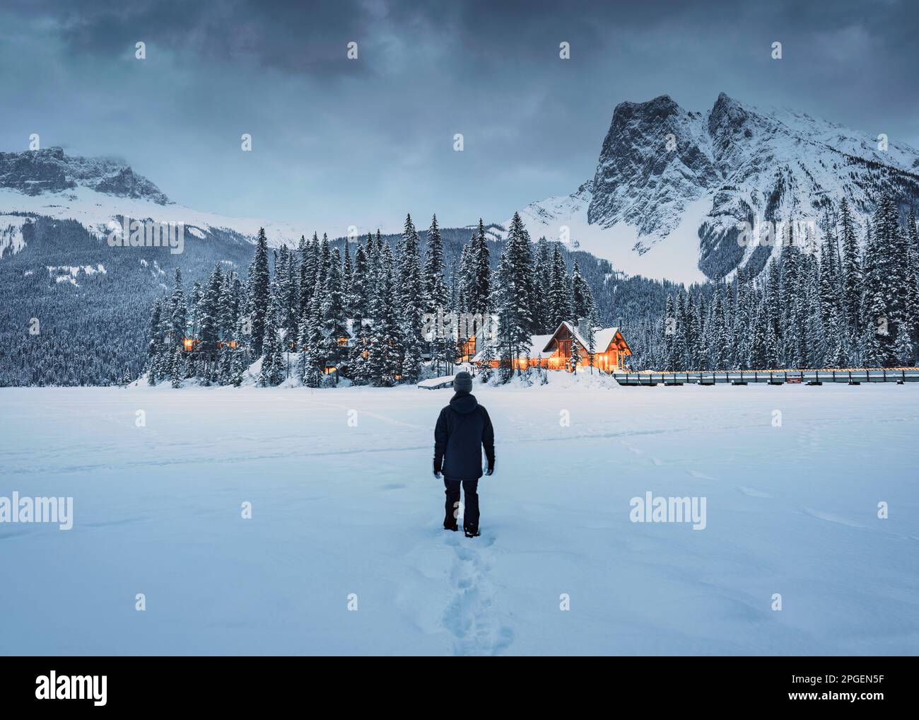 Un viaggiatore in piedi in campo di neve con loggia di legno incandescente e pineta in montagne rocciose al parco nazionale di Yoho, Alberta, Canada Foto Stock